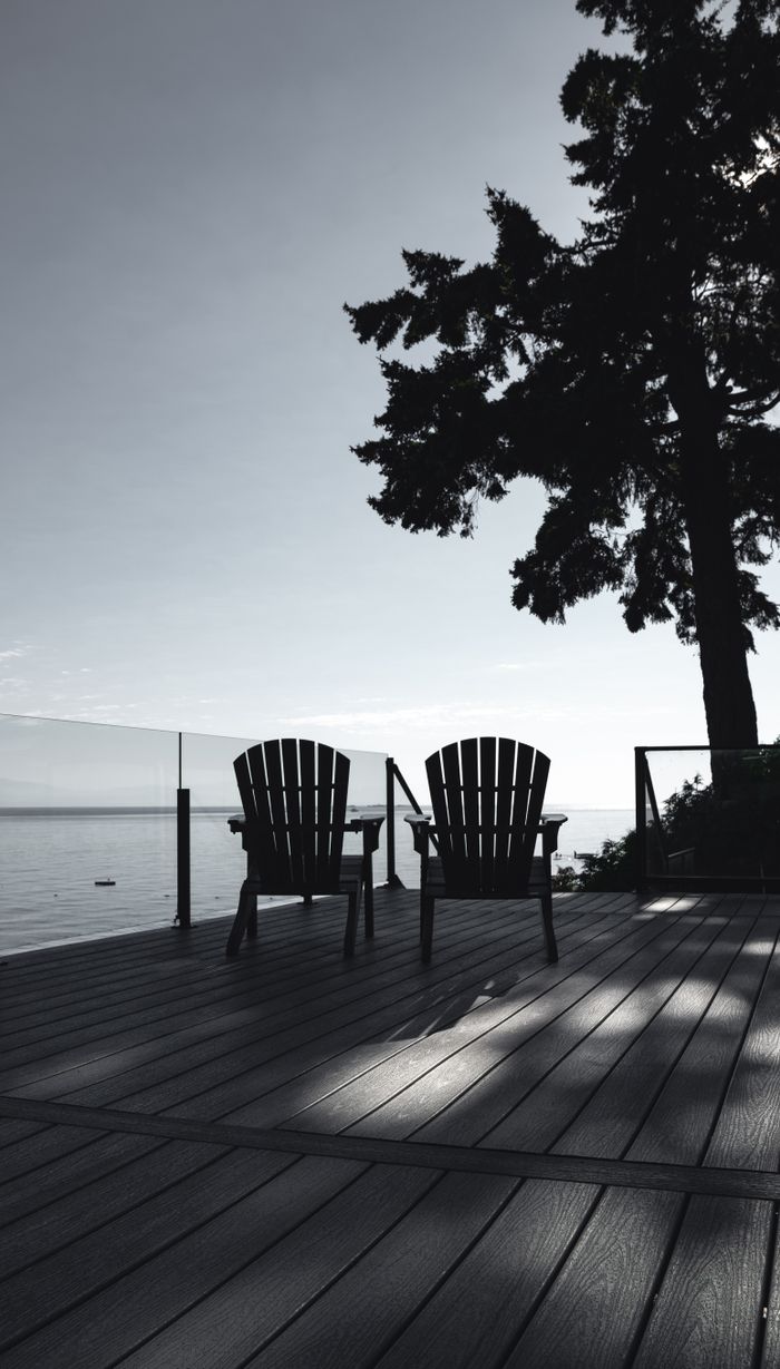 Two wooden chairs on a sunlit terrace by the sea, offering serene ocean views in Gibsons, BC.