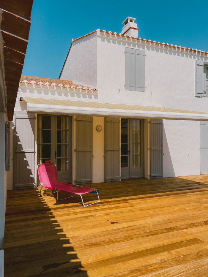 A serene terrace in France with a sunlit sunbed against a white wall under a blue sky.